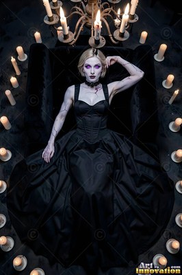 In a black corset dress, a pale woman lies resting inside a ring of lit candles