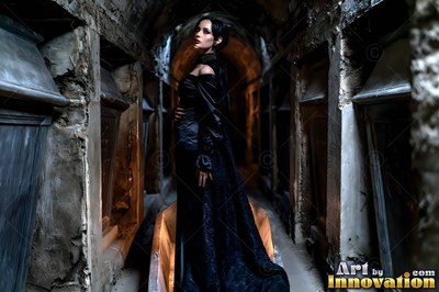 In a stone crypt, a fair woman in a long black gown looks over her shoulder