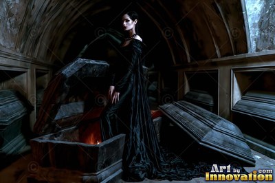 Woman in a long black gown stepping out of a stone coffin in a crypt