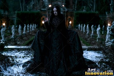 Standing facing forward in a dark garden, a woman wears a wide black gown
