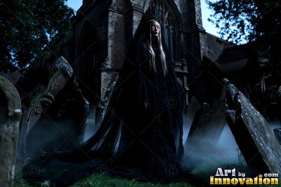 A woman in a long black veil and crown stands in a foggy churchyard at night