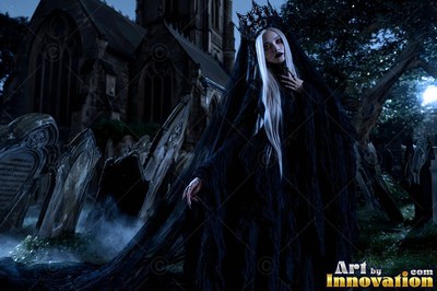 Standing in a misty graveyard, a woman in a black gown wears a dark crown and veil