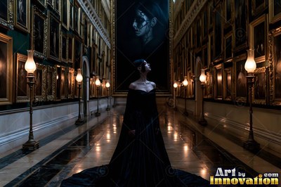 A woman in a black gown walks down a dark hall lit by soft lamp light