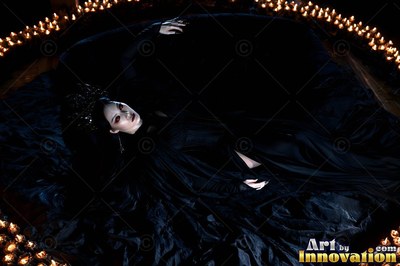 A woman dressed in a black gown lies inside a ring of burning candles