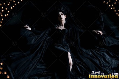 Black corset worn by a pale-skinned woman reclining in a flowing dark gown bordered by candle flames