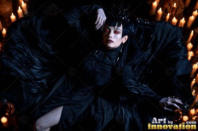 Reclining in a black dress, a woman with pale skin rests among warm candlelight