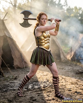 A red-haired woman wearing gold armor holds a large axe near camp tents