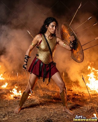 A woman in gold armor blocks flying arrows with her shield by a field of fire
