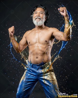 Standing with fists raised in a dark studio, a shirtless man is splashed with blue liquid