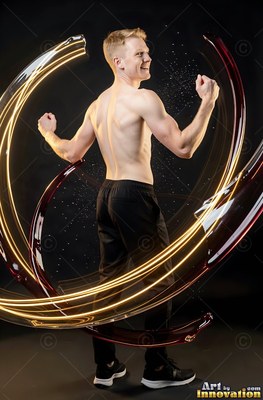 In a dark studio, a shirtless man flexes his arms inside swirls of liquid light