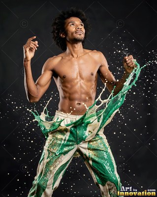 A shirtless man looks up as green and white paint splashes off his pants
