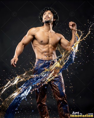 A shirtless man poses as splashes of blue and gold water arc across his body in studio light