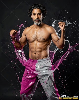 Raising clenched fists, a shirtless man stands as pink and white liquid splashes past him