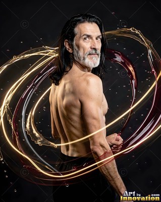 In a dark studio, a shirtless older man turns as rings of liquid swirl around him