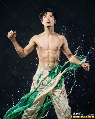 In a dark studio, a shirtless man poses as green and white paint splashes on him