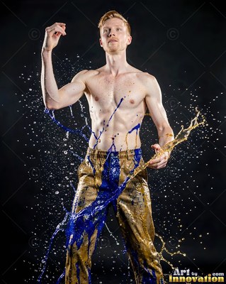 A shirtless man poses as splashes of blue paint and clear water fly past him