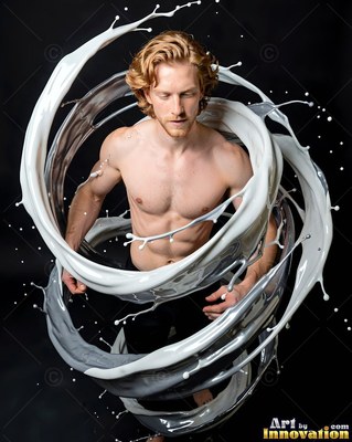 Standing in a dark studio, a shirtless man is encircled by white liquid splashes