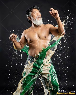A shirtless bearded man poses as green and cream paint splashes over him