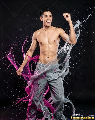 In a dark studio, a shirtless man dances as pink paint and water splash around him