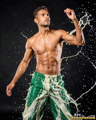 Bright green pants on a shirtless man dodging flying white liquid in a dark studio