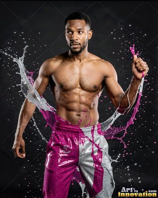 A shirtless man poses as water and pink paint splash around his shorts in bright white light