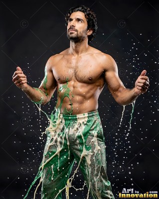 A shirtless man in green pants looks up as white and green liquid splashes on him
