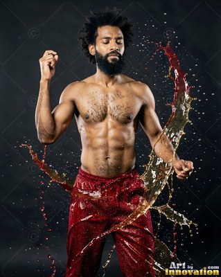 Posing with eyes closed, a shirtless bearded man stands in splashing liquid