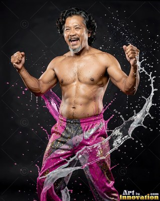 A shirtless man in pink pants shouts happily while water splashes around him