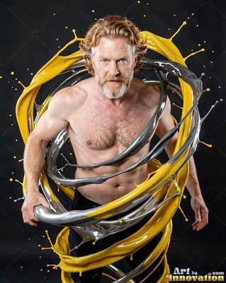 Red-bearded shirtless man wrapped in swirls of silver and yellow paint in a dark studio