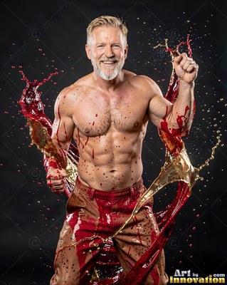 Front view of a shirtless man in a dark studio splashed with red liquid