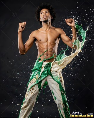 A shirtless man raises his fists as white and green liquid splashes over his pants