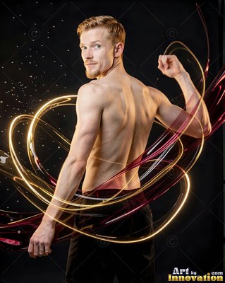 In a dark studio, a shirtless man flexes his arm wrapped in light and red ribbons