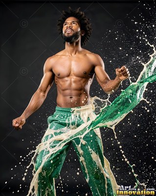 A shirtless man in green sweatpants gets hit by a splash of green and white paint