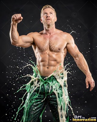Green pants splash white fluid on a shirtless man in a dark studio