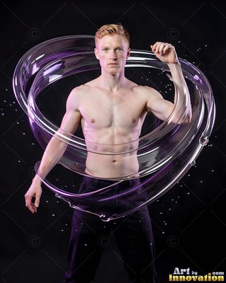 In a dark studio, a shirtless man is encircled by rings of clear water