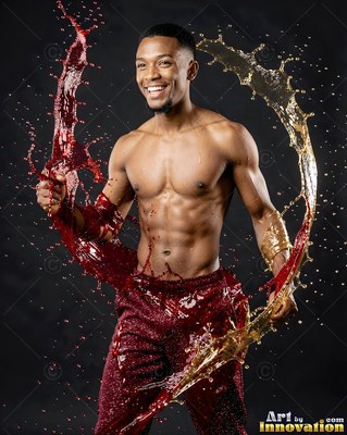 Smiling in a dark studio, a shirtless man swings splashes of red and gold liquid around him