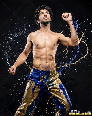 A shirtless man raises his fists as splashes of blue and gold liquid wrap around his pants