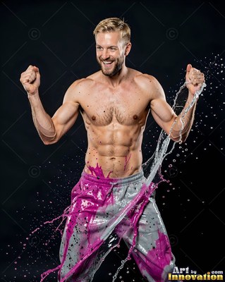Bare-chested man laughing in a dark studio while splashed with pink paint and water