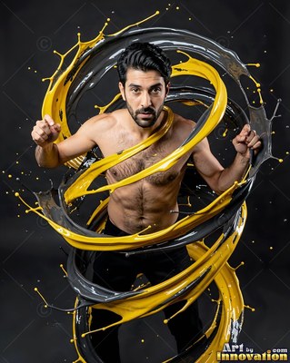 In a dark studio, a shirtless man is encircled by swirling yellow and gray paint