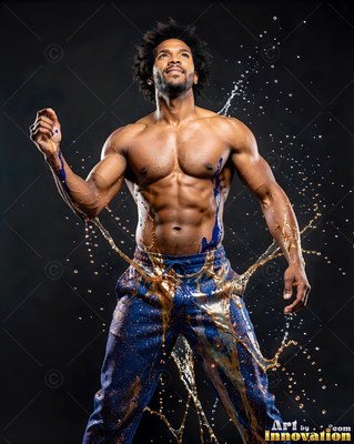 A muscular man stands looking up as liquid splashes off his blue pants in clear light