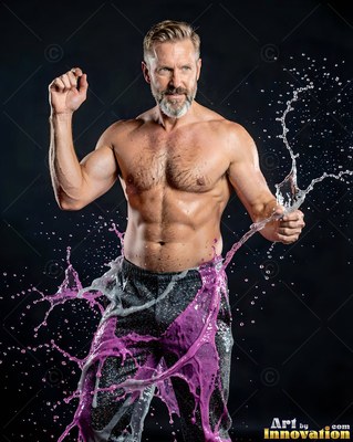 In a dark studio, a shirtless man poses as purple water splashes on his legs