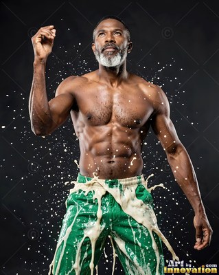 A gray-bearded man in green pants stands in a dark studio as cream-colored liquid splashes over him