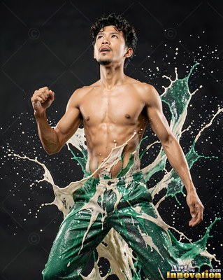 In a dark studio, a shirtless man looks up as white and green liquid splashes around him