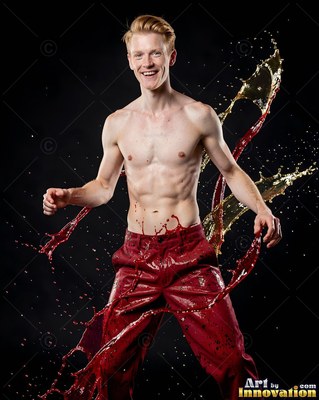 A smiling shirtless man in red pants dodging splashes of fluid