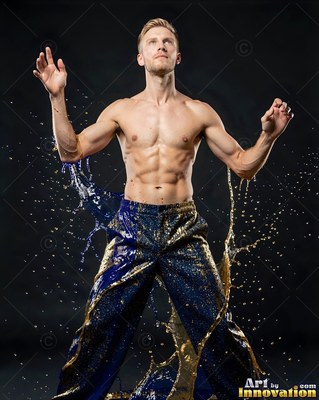 A shirtless man raises his hands as blue and gold water splashes up his legs