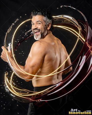 In a dark studio, a shirtless man smiles inside rings of splashing liquid