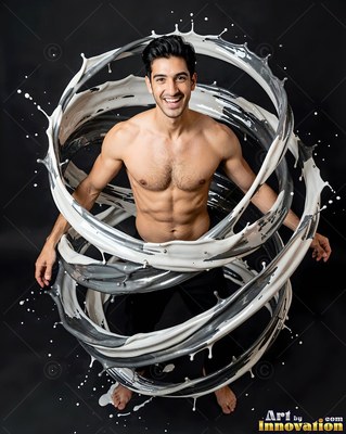A shirtless smiling man stands in a dark studio wrapped in a swirl of white and gray liquid splashes
