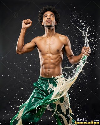 Jumping upward, a shirtless man in green pants kicks through splashing milk