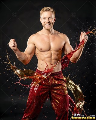 Wearing red sequined pants in a dark studio, a shirtless man flexes as red and gold liquids splash around him