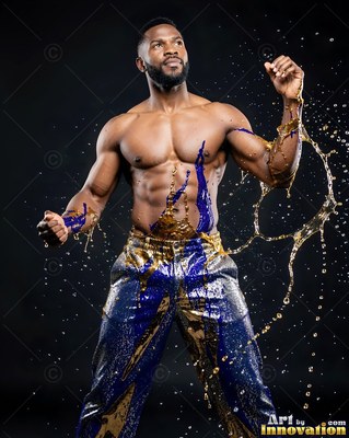 Standing in a dark studio, a shirtless man flexes as gold water splashes around him
